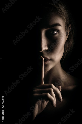 The girl shows a sign of silence. Face on black background, close-up photo