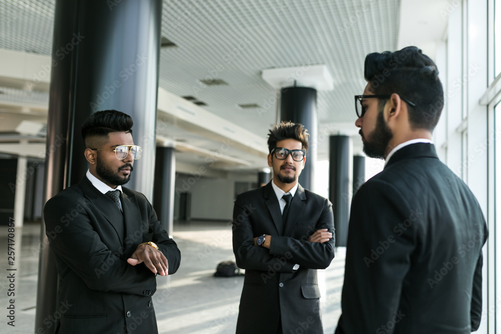 Indian business partners standing in office building and discussing work Indian business partners standing in office building and discussing work