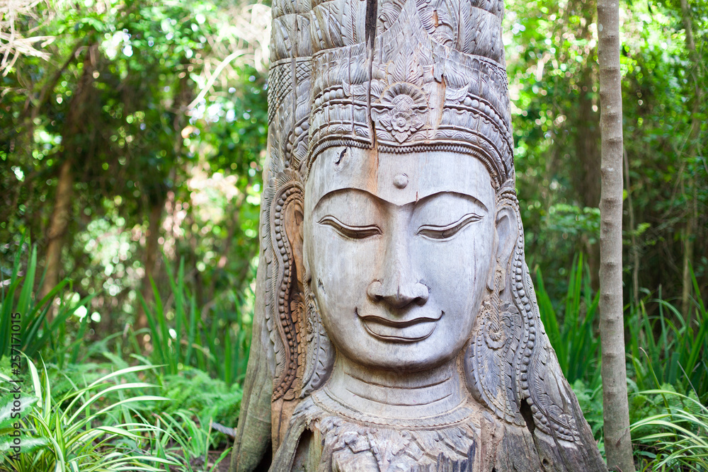 Wooden Buddha head statue with closed eyes on green trees forest background close up Wooden Buddha head statue with closed eyes on green trees forest background close up