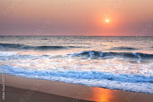 Fototapeta Naklejka Na Ścianę i Meble -  Stunning sunset or sunrise over the sea or ocean on the beach, purple sky, blue waves, white foam and golden sun reflection