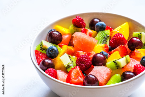 bowl of summer fruit and berry salad on white marble background. healthy vegan food