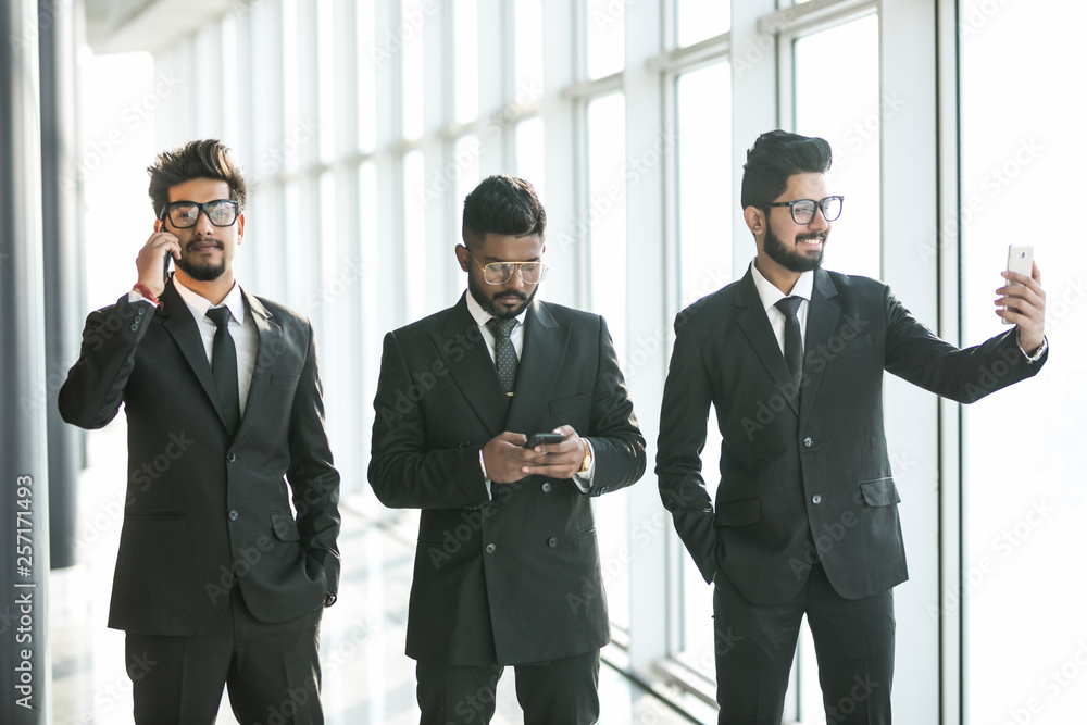 Young indian businessmen use phones for call, selfie or typing phone in modern office. Multitask use of phones. Young indian businessmen use phones for call, selfie or typing phone in modern office. Multitask use of phones.