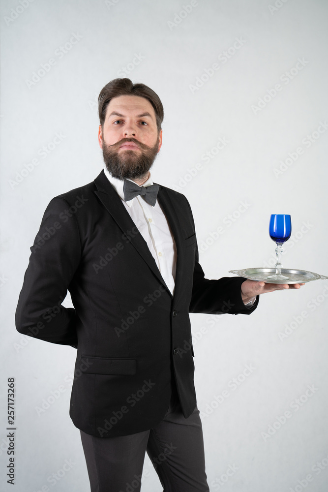 caucasian servant with a beard in a formal business suit stands with a steel tray in his hand and a glass of wine on a white solid background in the Studio caucasian servant with a beard in a formal business suit stands with a steel tray in his hand and a glass of wine on a white solid background in the Studio