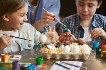 Cropped shot of two cute kids painting easter eggs with mom