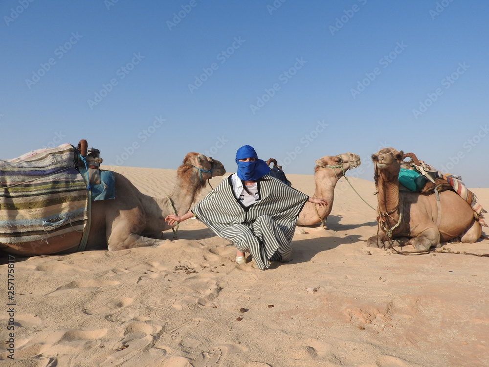 Fototapeta premium the woman in the turban, the face is closed, with a camel in the Sahara desert.
