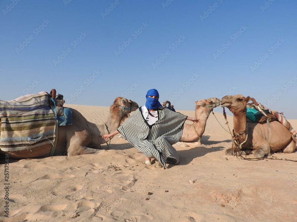 Fototapeta premium the woman in the turban, the face is closed, with a camel in the Sahara desert.