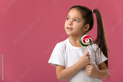 Beautiful cute little child girl with sweet candy lollipop isolated on pink background