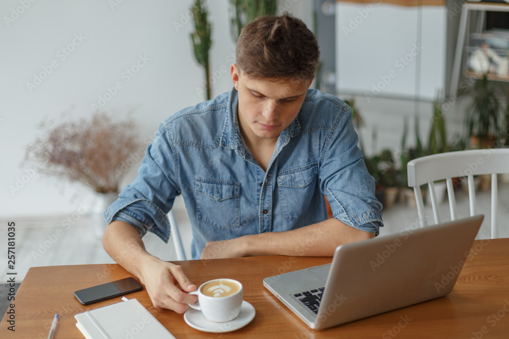 A young man works at a laptop in a cozy cafe. The concept of a freelacer workspace. A young man works at a laptop in a cozy cafe. The concept of a freelacer workspace.