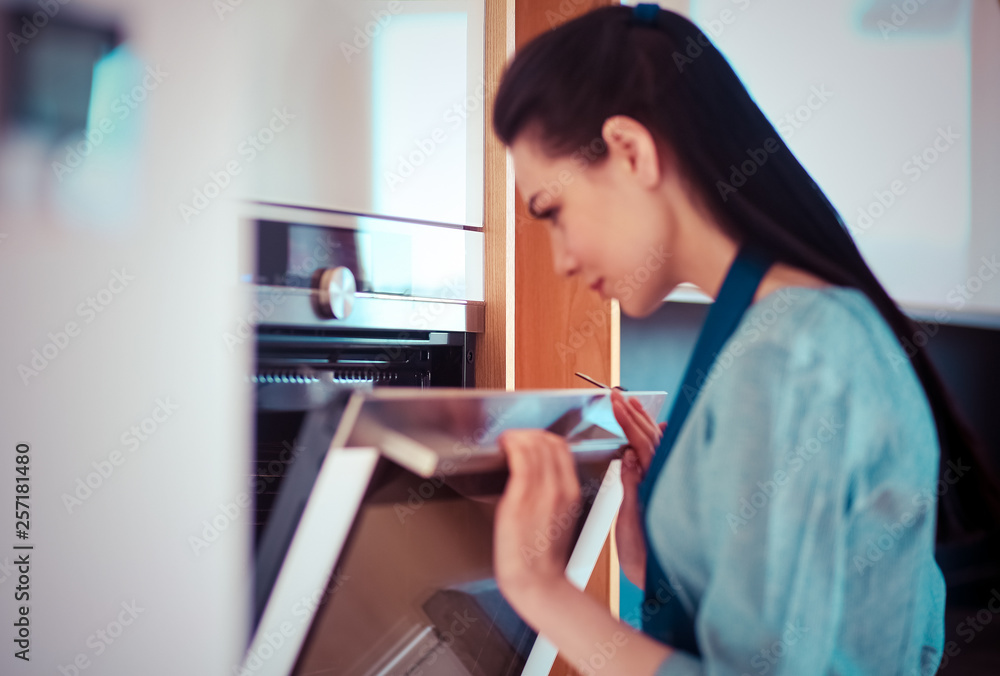 Beautiful young woman checking how her cake is doing in the oven Beautiful young woman checking how her cake is doing in the oven