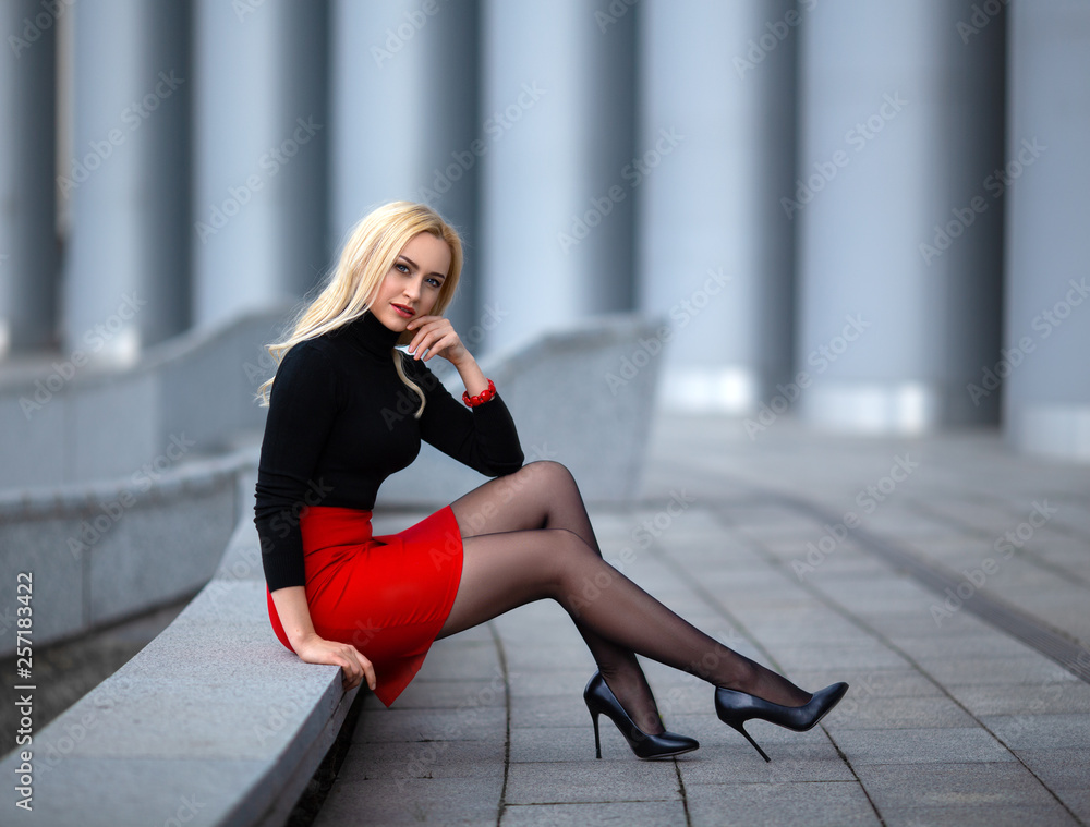 Beautiful blonde girl in red skirt with perfect legs in pantyhose and shoes  with high heels posing outdoor on the city square. Stock-Foto | Adobe Stock