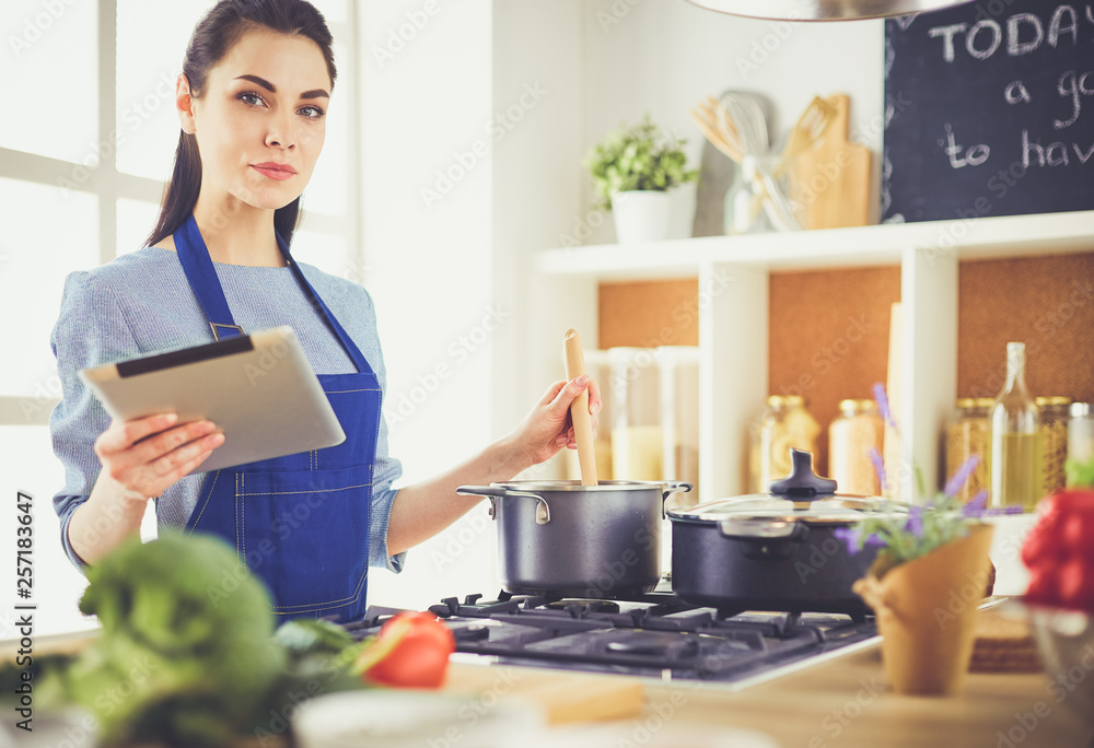 Young woman using a tablet computer to cook in her kitchen Young woman using a tablet computer to cook in her kitchen