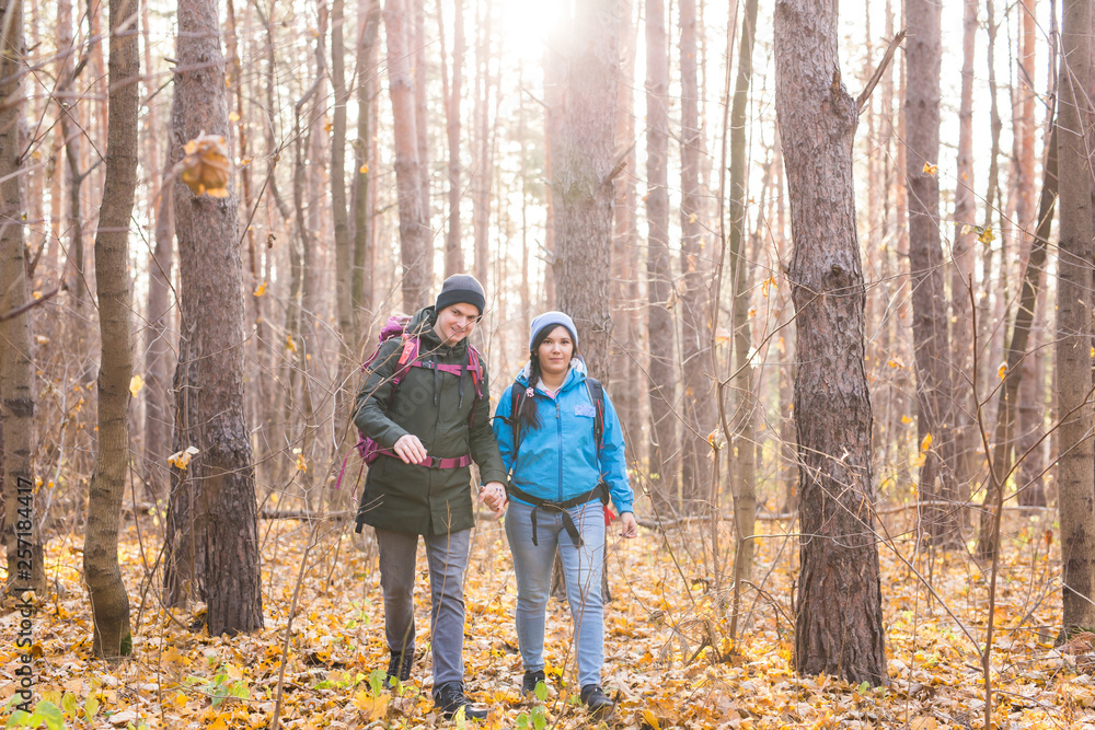 adventure, travel, tourism, hike and people concept - smiling couple walking with backpacks over autumn natural background