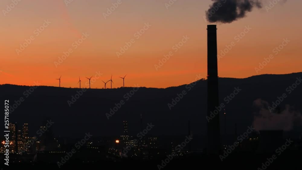 Smoking factory chimneys in sunset with wind turbine. Energy power stations, chemical factories and wind power stations. Global pollution concept, energy consumption. Smoking factory chimneys in sunset with wind turbine. Energy power stations, chemical factories and wind power stations. Global pollution concept, energy consumption.