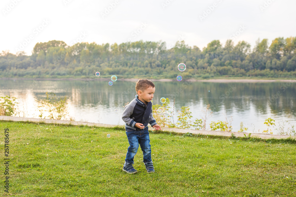 Chilhood, people concept - young boy playing with soap bubbles