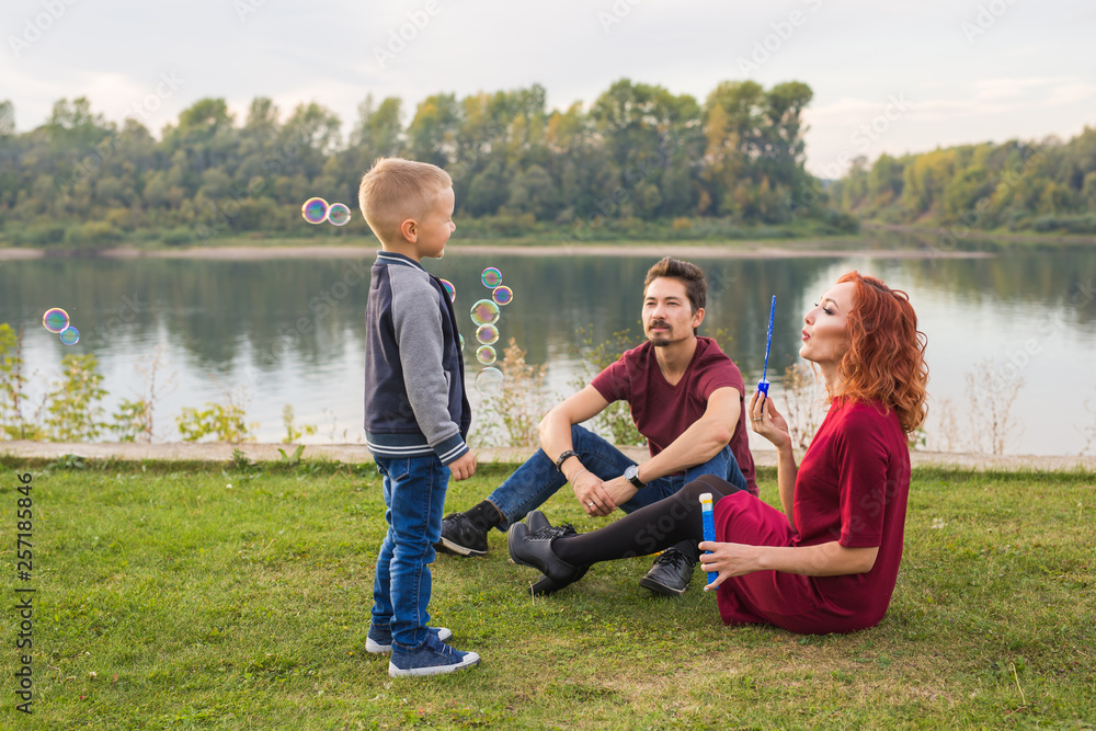 Family and nature concept - Mother, father and their child playing with colorful soap bubbles Family and nature concept - Mother, father and their child playing with colorful soap bubbles