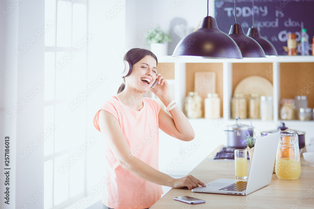 Young woman in kitchen with laptop computer looking recipes, smiling. Food blogger concept. Young woman in kitchen with laptop computer looking recipes, smiling. Food blogger concept.