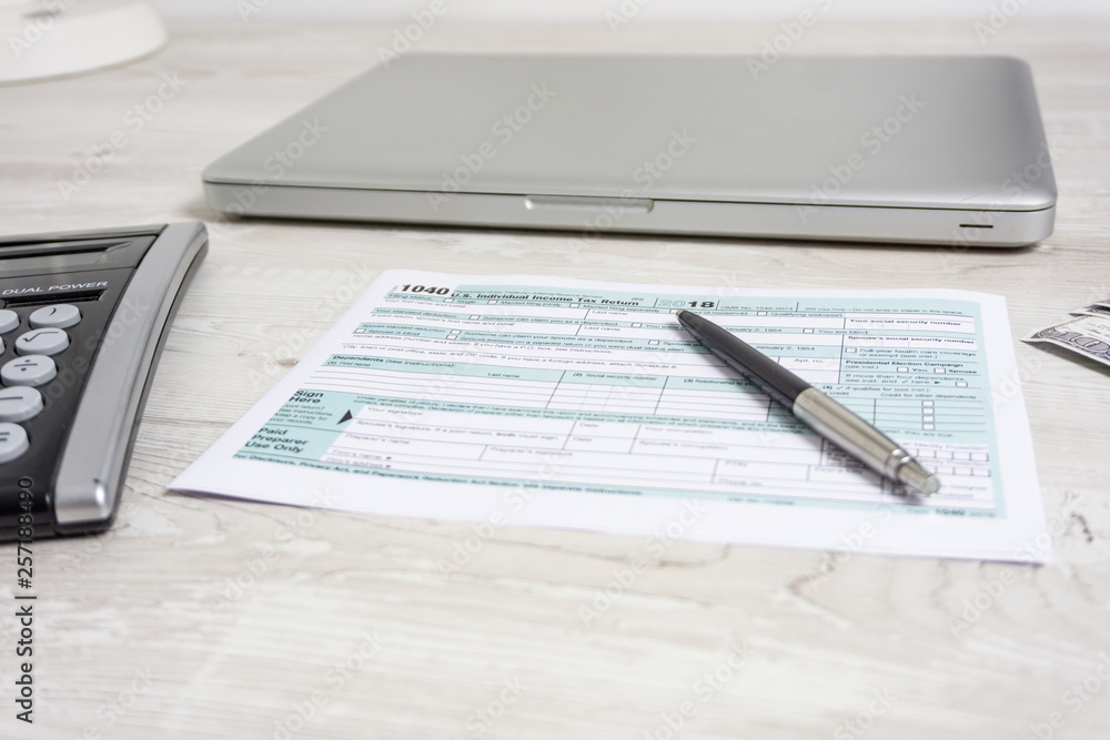 US tax form next to closed computer laptop, calculator and tax form 1040. tax form us business income office. Tax day 15th of April 2019 US tax form next to closed computer laptop, calculator and tax form 1040. tax form us business income office. Tax day 15th of April 2019