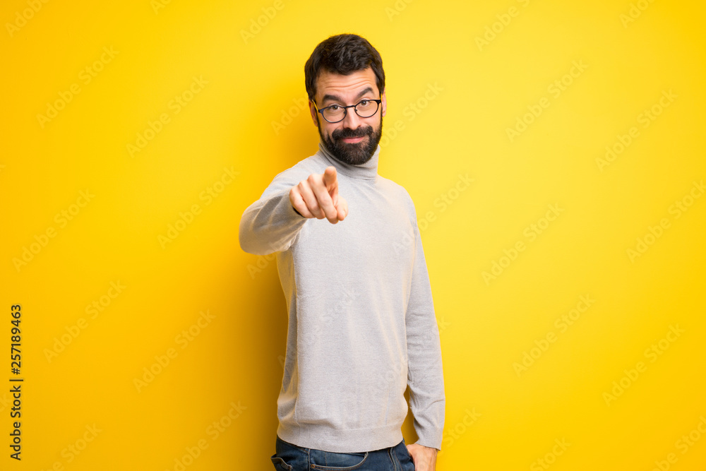 Man with beard and turtleneck points finger at you with a confident expression - obrazy, fototapety, plakaty 