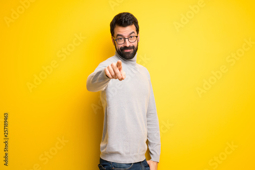 Man with beard and turtleneck points finger at you with a confident expression
