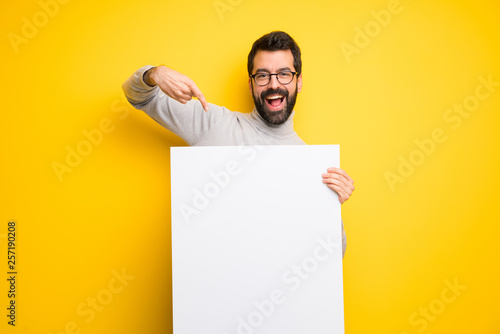 Man with beard and turtleneck holding an empty white placard