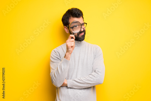 Man with beard and turtleneck taking a magnifying glass and looking through it