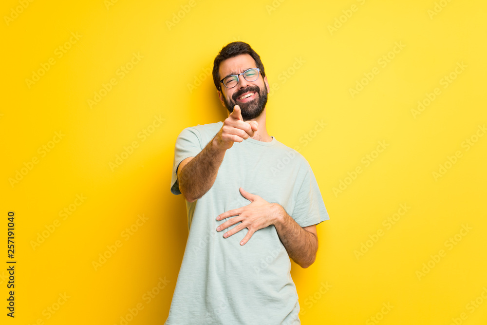 Man with beard and green shirt pointing with finger at someone and laughing a lot Man with beard and green shirt pointing with finger at someone and laughing a lot