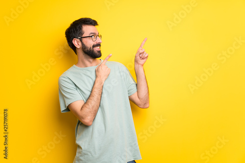 Man with beard and green shirt pointing with the index finger and looking up