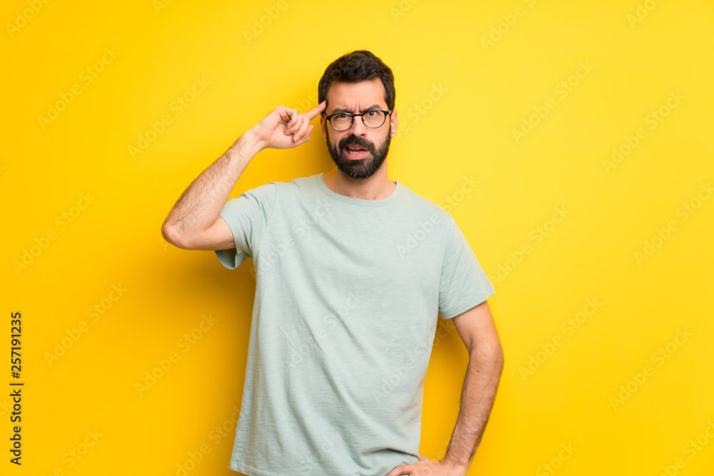 Man with beard and green shirt making the gesture of madness putting finger on the head Man with beard and green shirt making the gesture of madness putting finger on the head