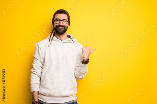 Hippie man with dreadlocks pointing to the side to present a product