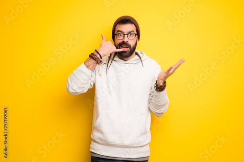 Hippie man with dreadlocks making phone gesture and doubting