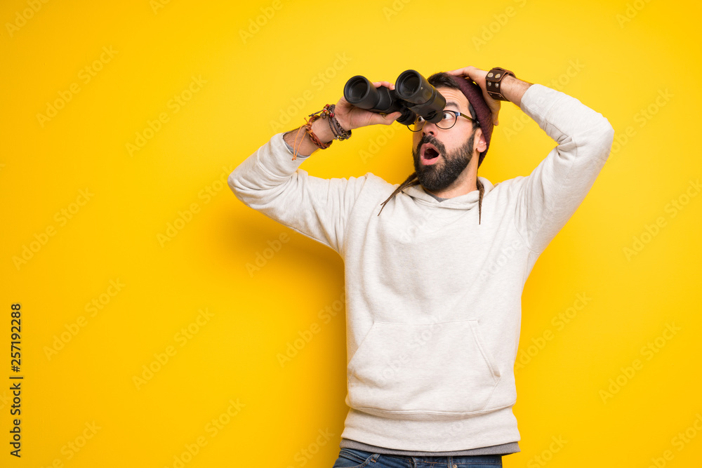 Hippie man with dreadlocks and looking in the distance with binoculars Hippie man with dreadlocks and looking in the distance with binoculars