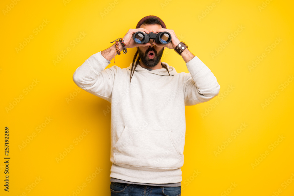 Hippie man with dreadlocks and looking in the distance with binoculars Hippie man with dreadlocks and looking in the distance with binoculars
