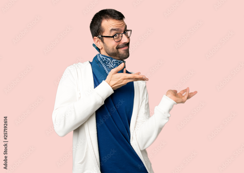 Handsome man with glasses extending hands to the side for inviting to come on isolated pink background Handsome man with glasses extending hands to the side for inviting to come on isolated pink background