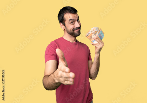 Man taking a lot of money shaking hands for closing a good deal on isolated yellow background