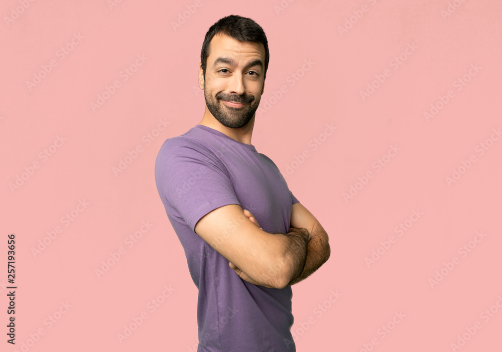 Handsome man keeping the arms crossed in lateral position while smiling on isolated pink background Handsome man keeping the arms crossed in lateral position while smiling on isolated pink background