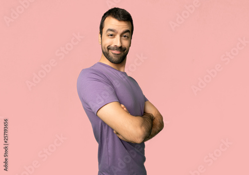 Handsome man keeping the arms crossed in lateral position while smiling on isolated pink background
