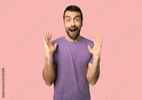 Handsome man with surprise and shocked facial expression on isolated pink background