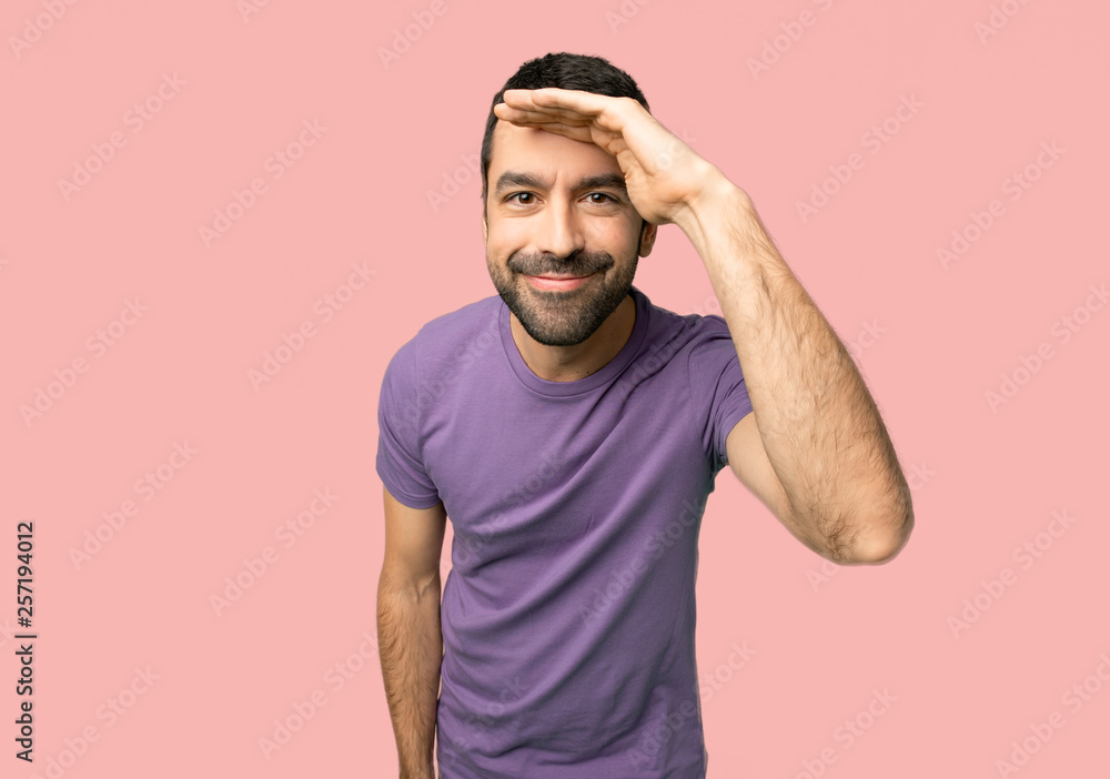 Handsome man looking far away with hand to look something on isolated pink background Handsome man looking far away with hand to look something on isolated pink background