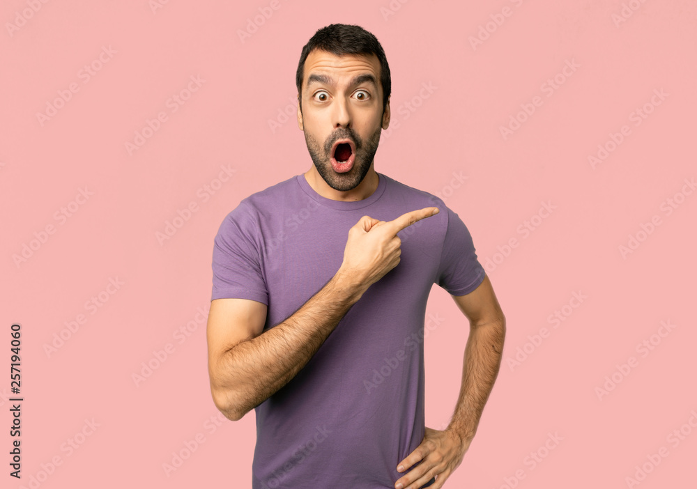 Handsome man surprised and pointing side on isolated pink background Handsome man surprised and pointing side on isolated pink background