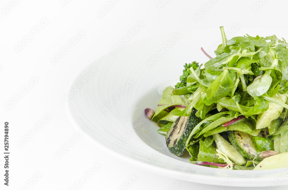 Salad of green vegetables with broccoli, zucchini and walnut dressing on a plate on a white background Salad of green vegetables with broccoli, zucchini and walnut dressing on a plate on a white background