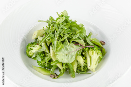 Salad of green vegetables with broccoli, zucchini and walnut dressing on a plate on a white background
