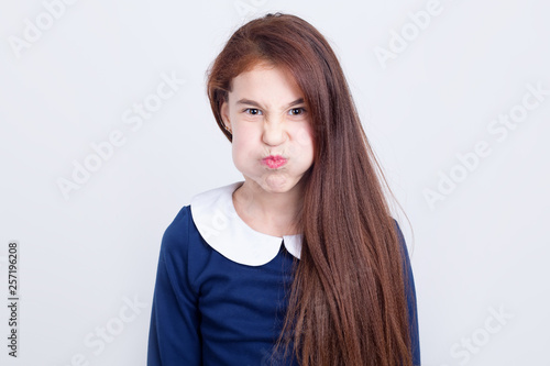 Portrait of a girl who puffed up her cheeks in anger and displeasure while standing on a light background. photo