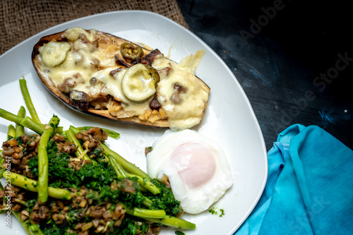 Baked eggplant with cheese and mushrooms, next to green legumes and spinach and fried egg