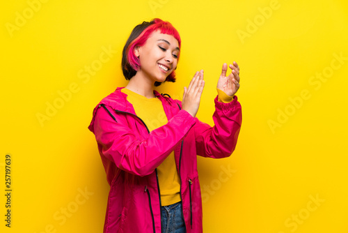 Young woman with pink hair over yellow wall applauding after presentation in a conference