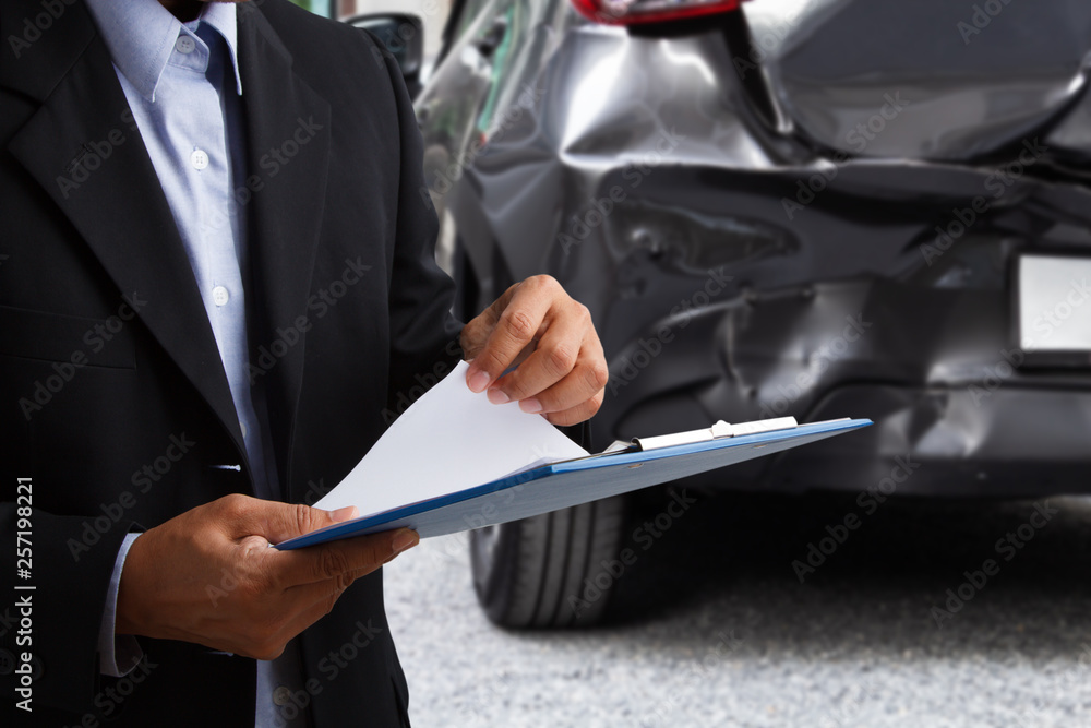 Insurance officer writing on clipboard while insurance agent examining car after acciden