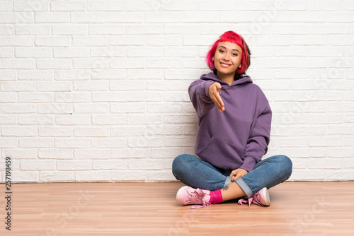 Young woman with pink hair sitting on the floor shaking hands for closing a good deal © luismolinero