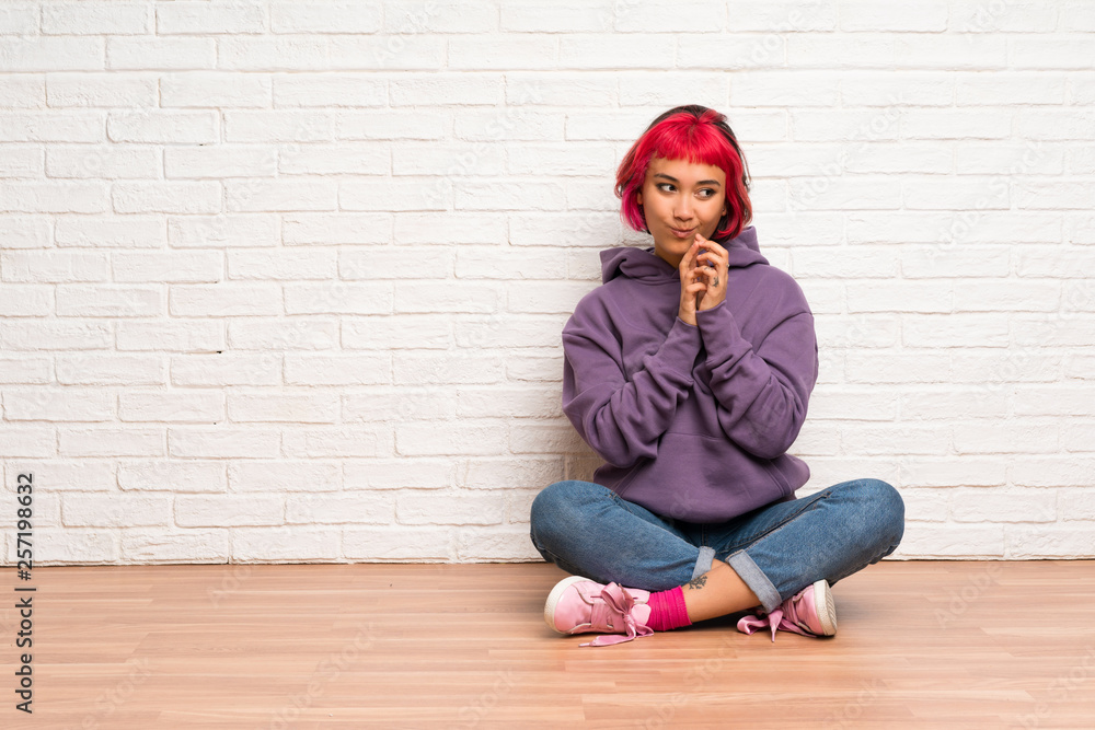 Young woman with pink hair sitting on the floor scheming something Young woman with pink hair sitting on the floor scheming something
