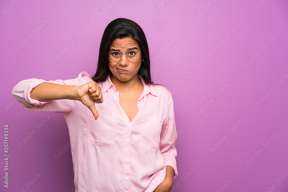 Young Colombian girl over purple wall showing thumb down sign Young Colombian girl over purple wall showing thumb down sign