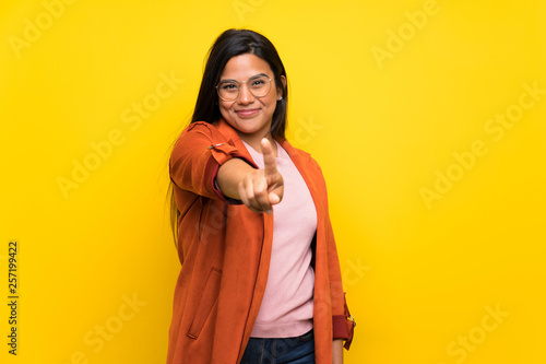 Young Colombian girl over yellow wall showing and lifting a finger © luismolinero