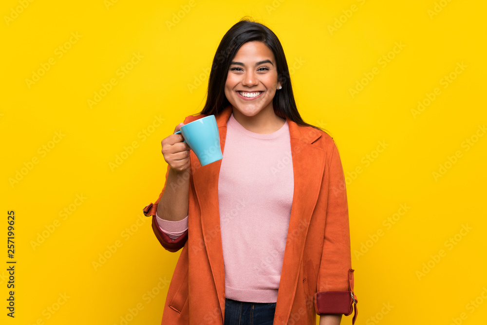 Young Colombian girl over yellow wall holding a hot cup of coffee Young Colombian girl over yellow wall holding a hot cup of coffee